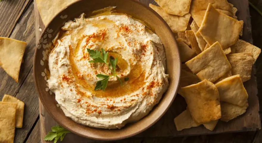 Houmous crémeux, garni de paprika et de persil, servi avec des chips pita croustillantes. Une recette houmous facile pour un apéritif gourmand.