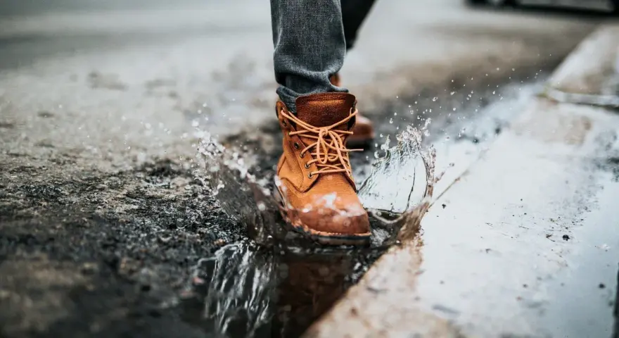 Botas de cuero marrón salpican un charco, demostrando que el cuero es impermeable.