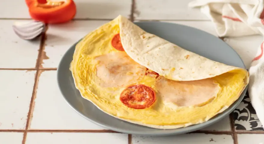 Pyszna tortilla z jajkiem, pomidorem i szynką, gotowa do zjedzenia.