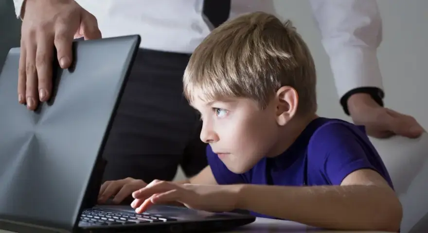 Chłopiec pochłonięty grą na laptopie, a dorosły próbuje pomóc w leczeniu uzależnienia od komputera.
