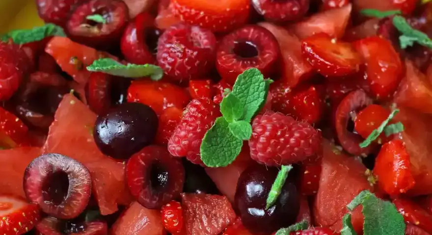 Macedonia di frutta fresca e colorata: fragole, ciliegie, lamponi e anguria, guarnita con foglie di menta.
