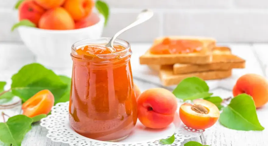 Tarro de mermelada de albaricoque casera, con tostadas y albaricoques frescos alrededor.