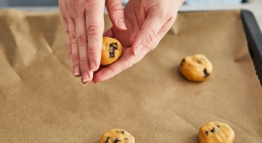 Hände formen Teig für einen Skillet Cookie mit Schokoladenstückchen auf Backpapier.