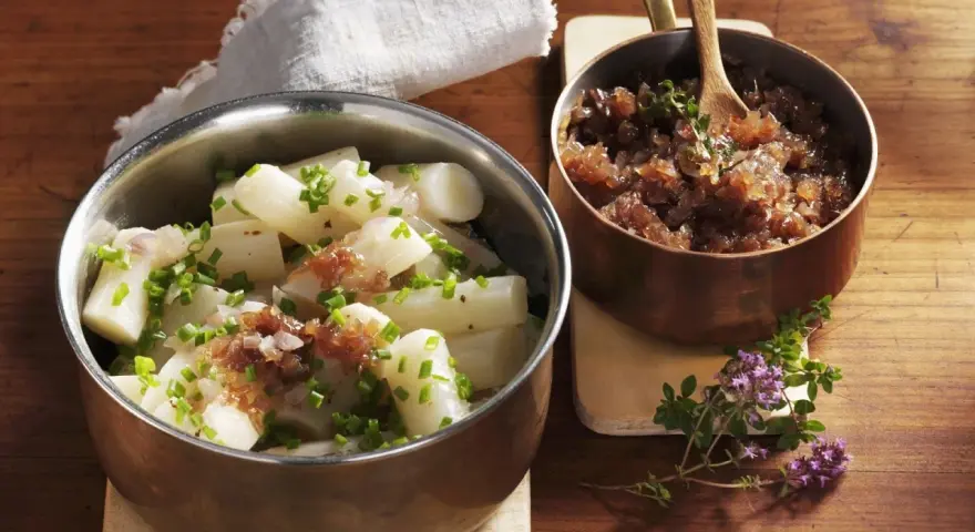 Ein köstliches Haferwurzel Rezept mit karamellisierten Zwiebeln und frischem Schnittlauch. Serviert in Kupfer- und Edelstahlschalen auf einem Holztisch.