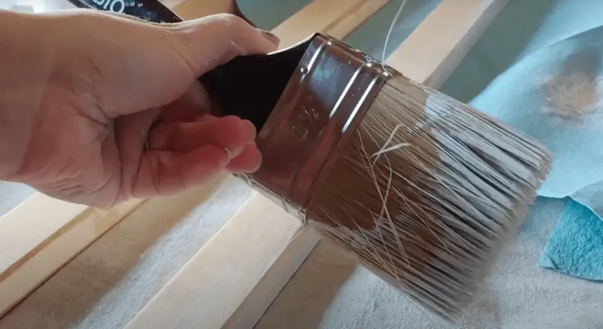 Mano aplica pintura con un pincel seco sobre listones de madera.
