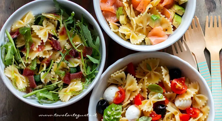 Tre ciotole di pasta fredda saporita: una con salmone e avocado, una con rucola e prosciutto, e una con pomodorini, mozzarelline e olive.