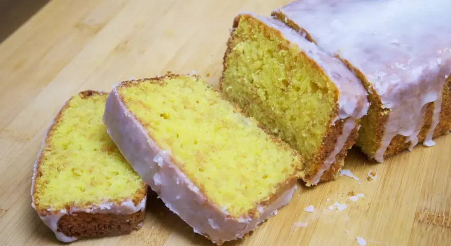 Un delicioso pastel de limón, cubierto con glaseado blanco, cortado en rebanadas sobre una tabla de madera.