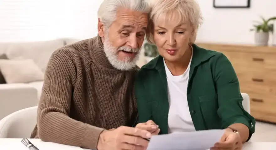 Starsze małżeństwo analizuje dokumenty przy stole.
