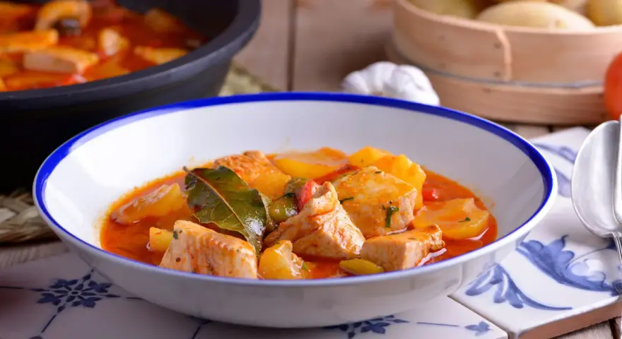 Bol de patatas con bonito en salsa roja, decorado con hojas de laurel.