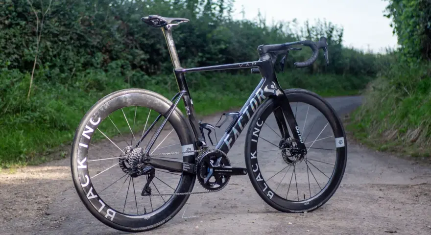A black Factor Ostro VAM road bike with Black Inc wheels sits on a dirt path, ready for an adventure.