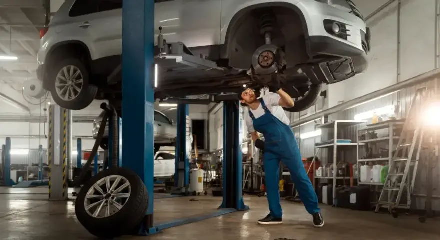 Mechanik pracuje pod samochodem na podnośniku. Szacowany koszt budowy warsztatu 100m2.