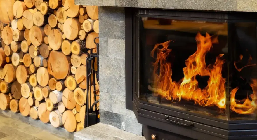 Leña apilada junto a una moderna insert chimenea con llamas danzantes.