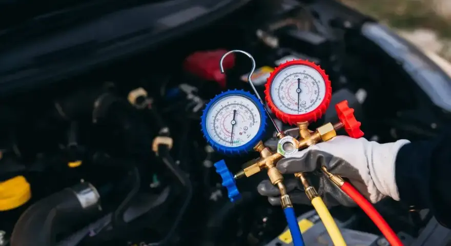 Profesjonalny serwis klimatyzacji samochodowej. Mechanik z manometrami sprawdza układ chłodzenia silnika.