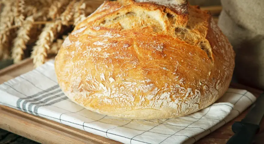 Ein knuspriges, schnelles Brot mit Backpulver, das auf einem karierten Tuch liegt. Im Hintergrund sind Ähren und ein Sack zu sehen.