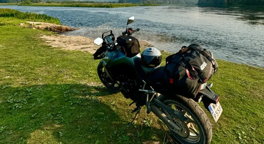 Motocykl z bagażem nad rzeką, gotowy do podróży po Litwie. Przepisy drogowe to podstawa bezpiecznej wyprawy.