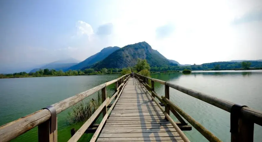 Ponte in legno su lago calmo, montagne verdi sullo sfondo. Un luogo incantevole per scoprire cosa vedere in Franciacorta, tra natura e tranquillità.