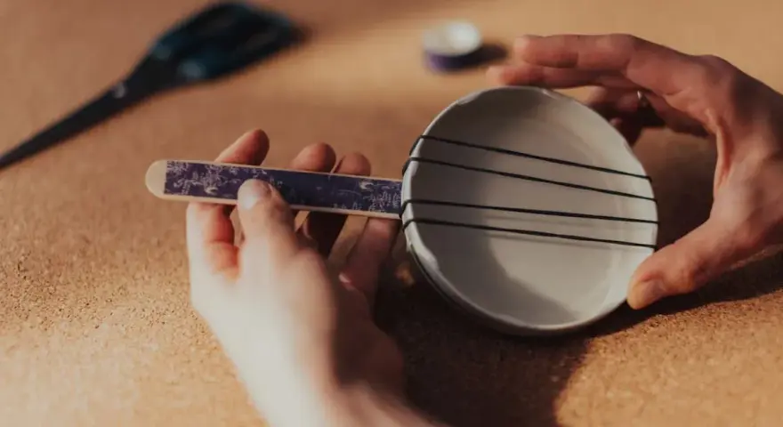 Dłonie tworzą domowy instrument strunowy, pokazując, jakie są instrumenty szarpane.