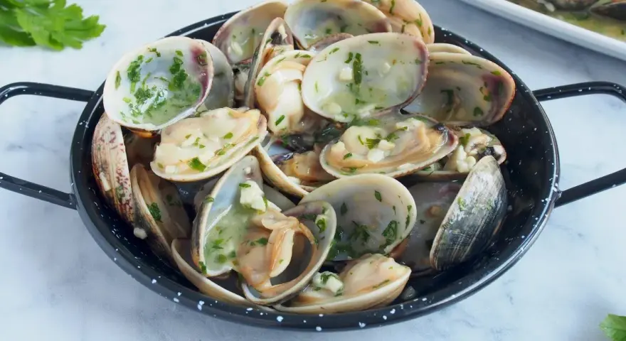 Almejas en salsa verde, un plato delicioso con mariscos frescos y perejil picado, listo para disfrutar.