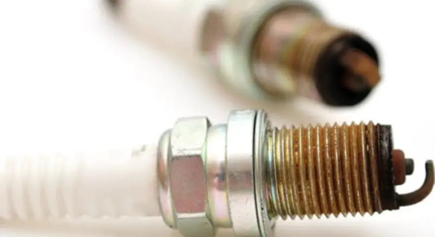 Two used spark plugs for cars, showing wear and tear on their metal tips.