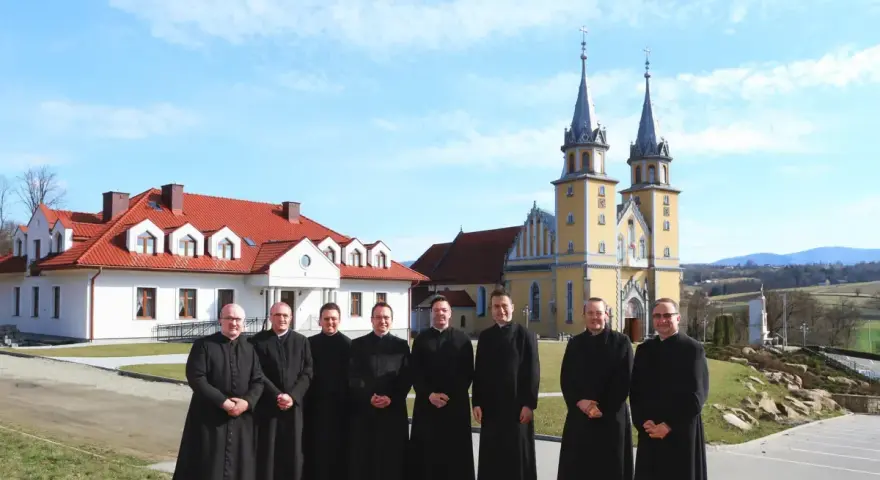 Grupa księży w czarnych szatach przed żółtym kościołem. Czy to miejsce, gdzie zbierany jest podatek na kościół?