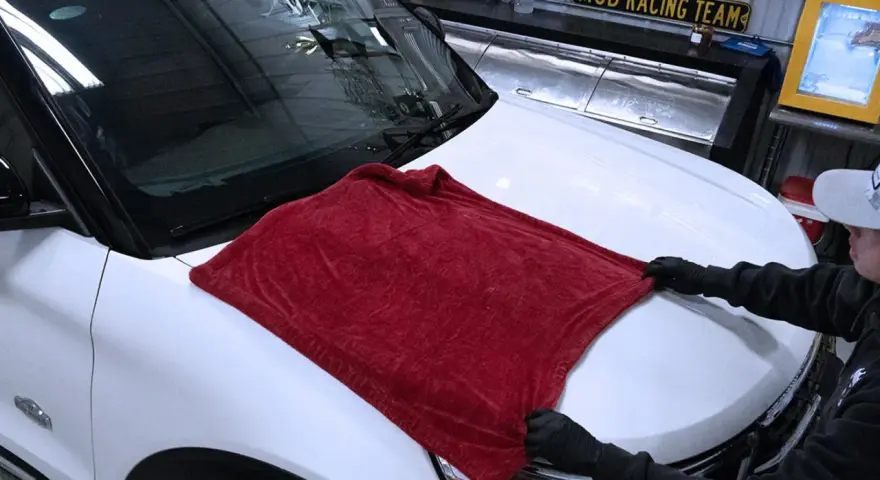 Person in gloves carefully places a plush red towel on a white car hood, demonstrating the best way to wash a car without scratching.