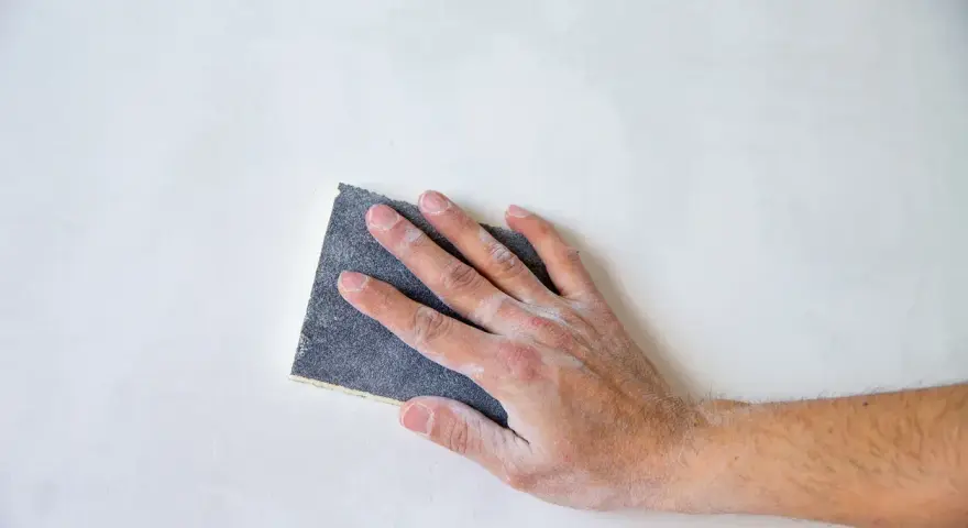Mano che leviga una superficie bianca con carta vetrata per legno, quale usare per un lavoro perfetto.