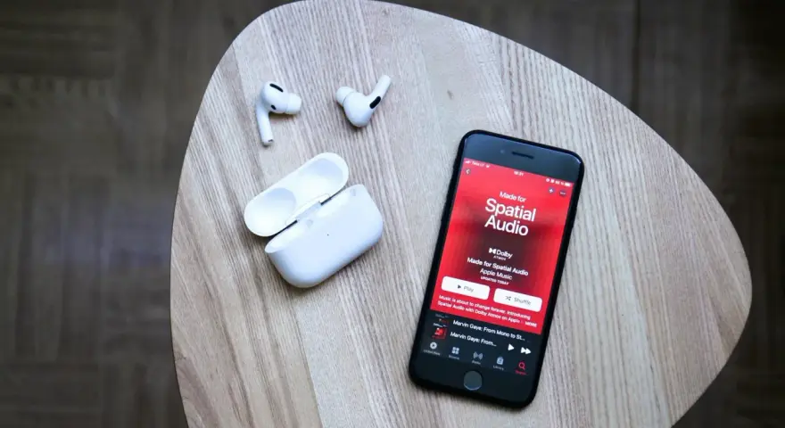 iPhone mit Apple Music Update zeigt "Made for Spatial Audio". AirPods und Ladecase liegen daneben.