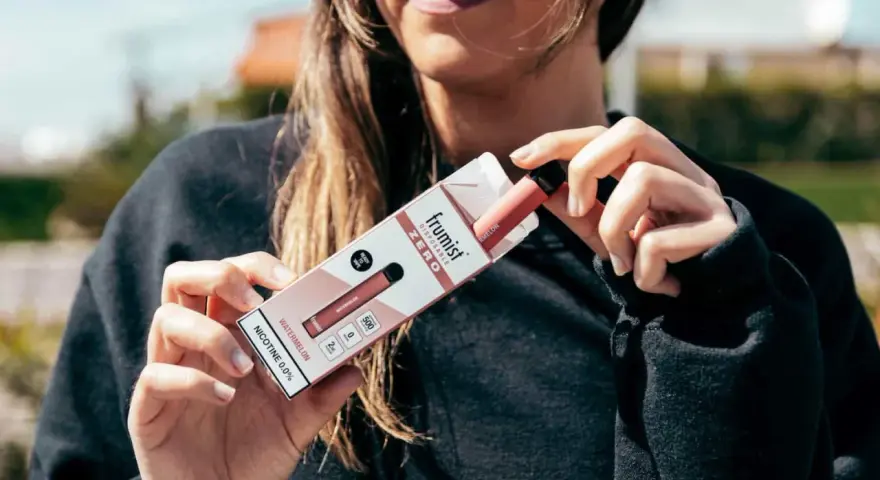 Mujer sosteniendo la caja de un vape desechable sabor sandía, sin nicotina.