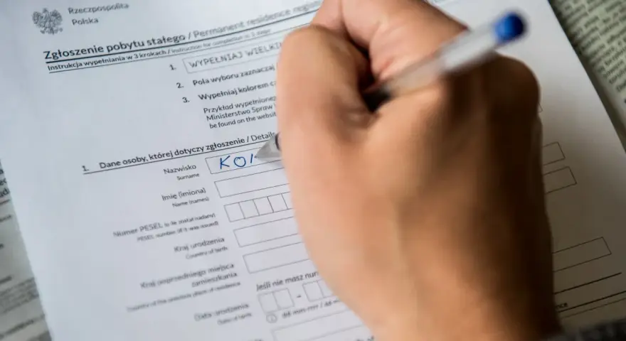 Ręka wypełnia formularz "Zgłoszenie pobytu stałego". Czy jest obowiązek meldunku? Tak, ten dokument to potwierdza.