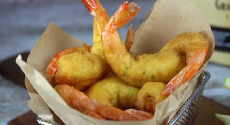 Crujientes gambas a la gabardina doradas y sabrosas, servidas en una cesta metálica con papel de cocina.