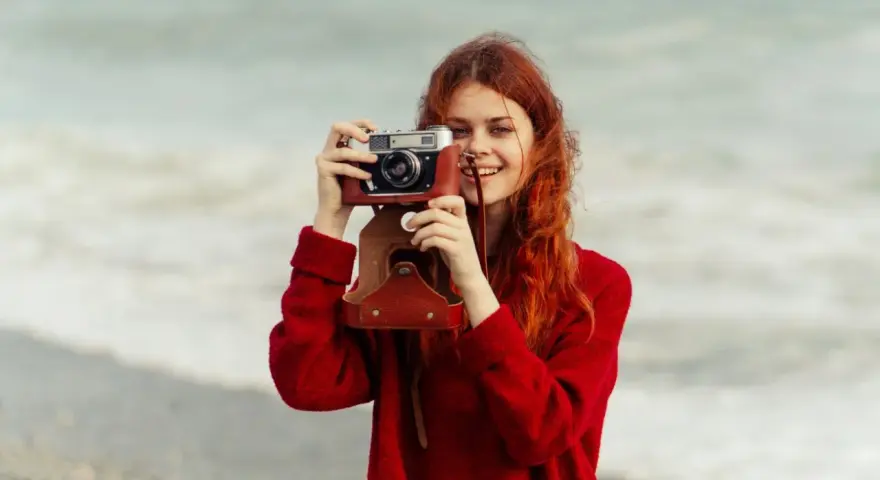 Ruda dziewczyna z aparatem, jak znani fotografowie, uwiecznia piękno morza.