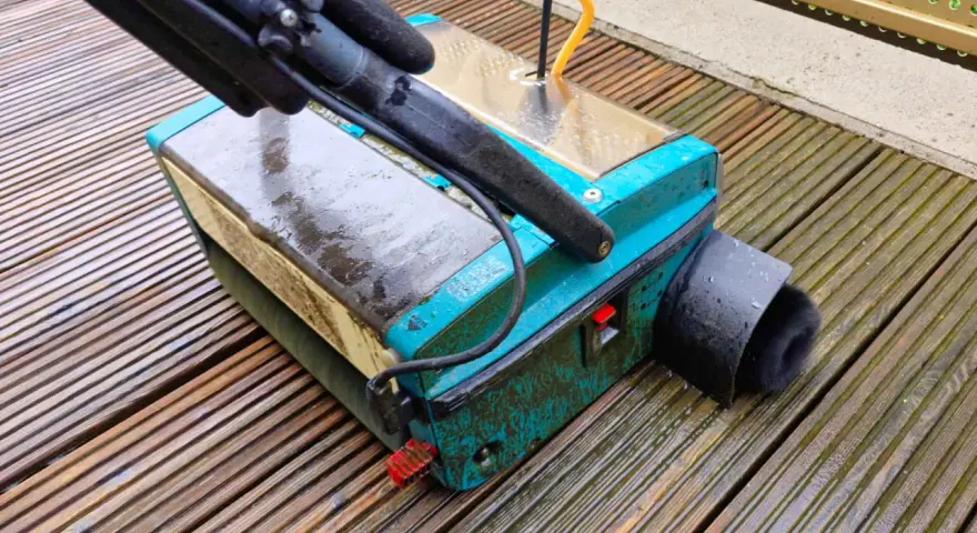 Gerät zur Bankirai Terrasse reinigen mit Bürstenaufsatz auf nassen Holzbrettern.