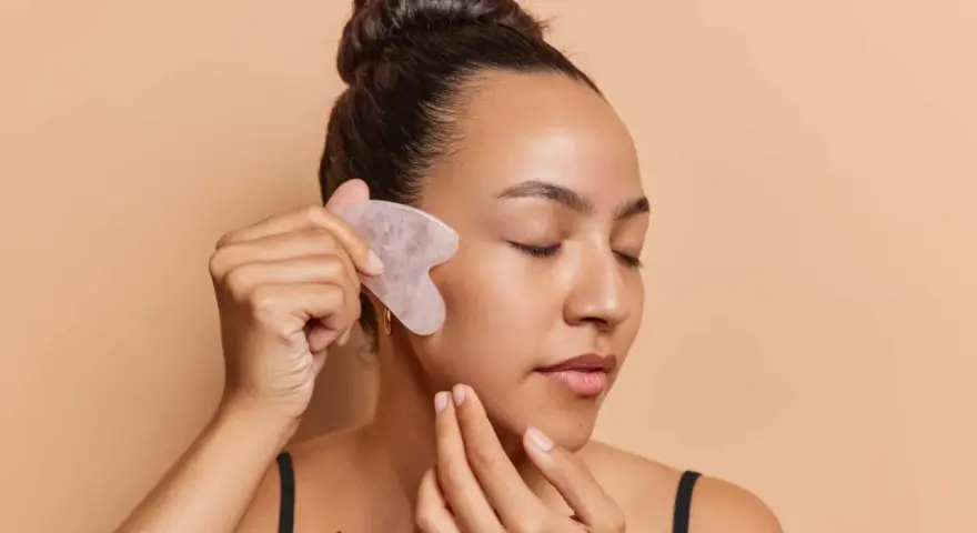 Frau mit geschlossenen Augen nutzt ein Gua Sha Stein zur Gesichtsmassage. Ob morgens oder abends, die Anwendung belebt die Haut.