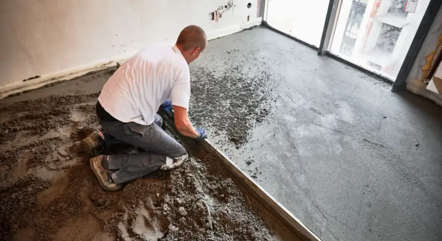 Budowlaniec wyrównuje świeży, suchy beton na posadzkę za pomocą łaty.