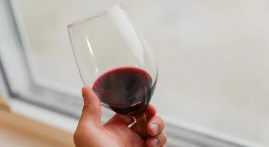 Dłoń trzyma kieliszek czerwonego wina. Czy wino jest zdrowe? To pytanie nurtuje wielu miłośników tego trunku.