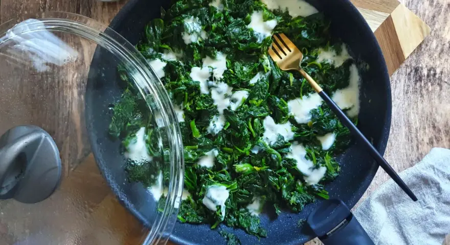 Spinaci in padella cremosi, con una forchetta dorata pronta ad assaggiarli. Un contorno semplice e gustoso.