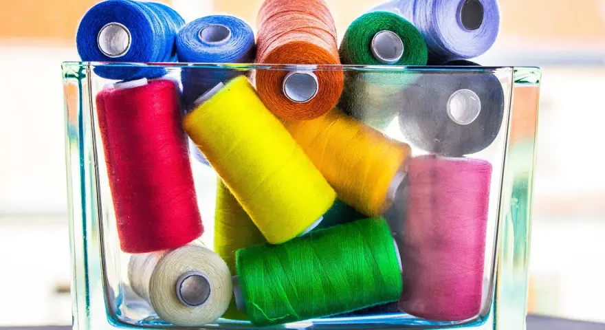 Un assortiment coloré de bobines de fil coton ou polyester, empilées dans un pot en verre.