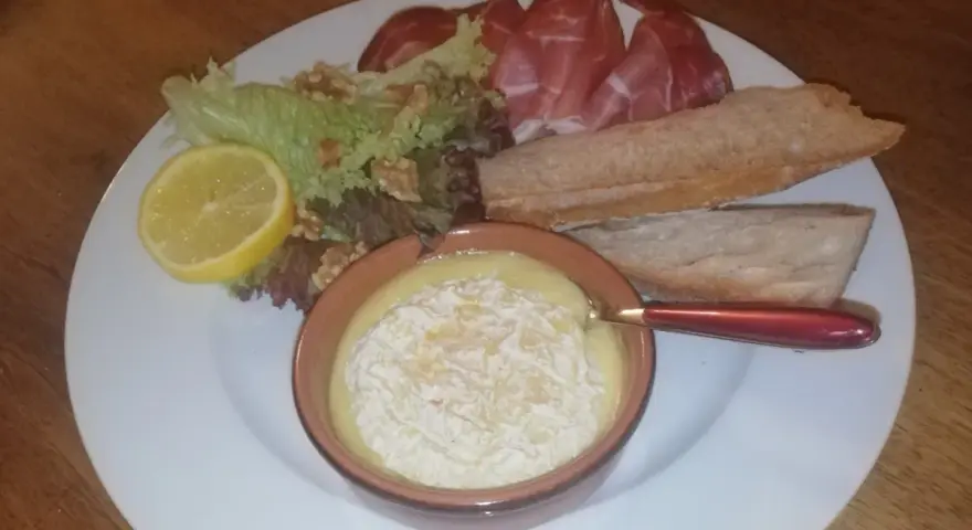 Un plat avec un fromage fondant, des tranches de jambon, de la salade, des noix, une tranche de citron et du pain. Une idée de recette amuse bouche facile sans cuisson.