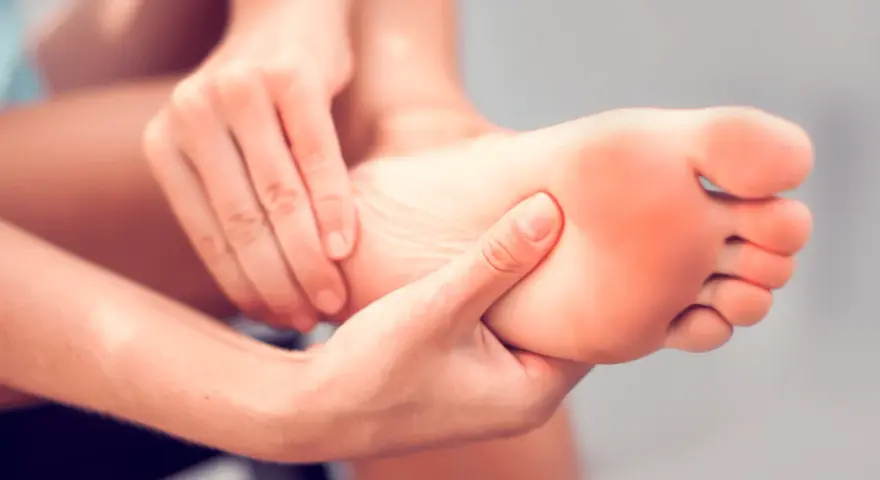 Hands massaging a foot, seeking aching feet remedy. The sole of the foot shows a slight red hue, indicating discomfort.