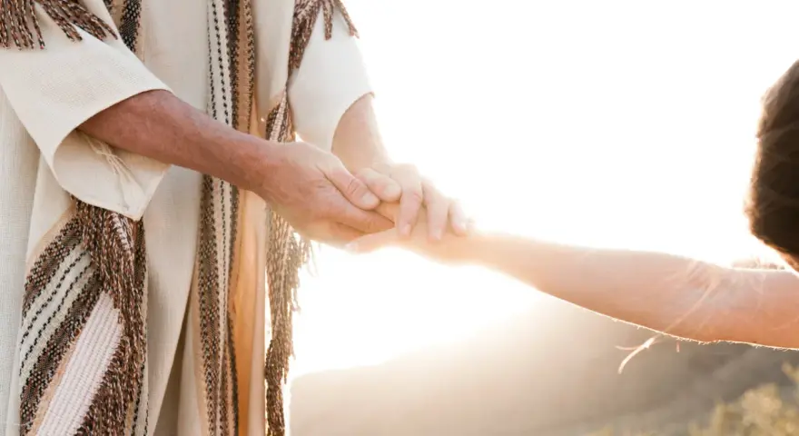 A person in a robe holds another's hand, symbolizing how to surrender to God through trust and guidance.