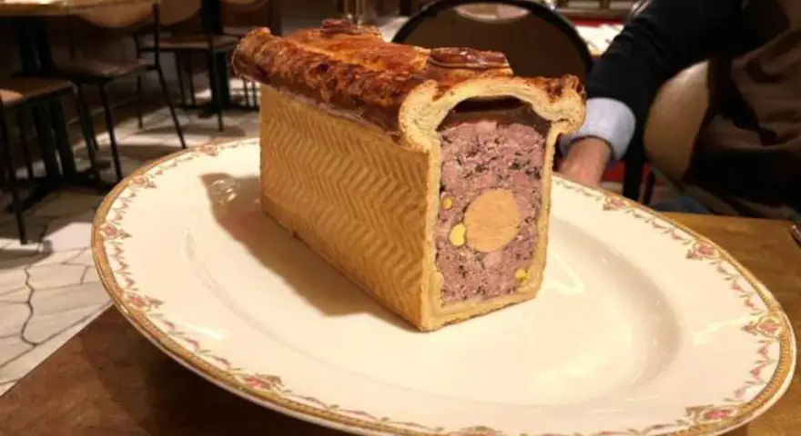 Un delicioso pâté de paques, un pastel de carne con un centro de foie gras, servido en un plato elegante.