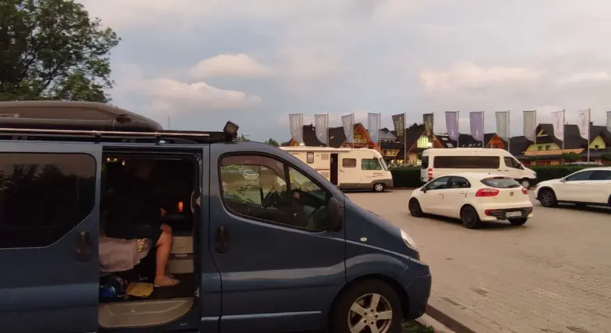 Na parkingu przy Chochołowskich Termach stoi ciemnoniebieski bus, biały samochód i kamper.