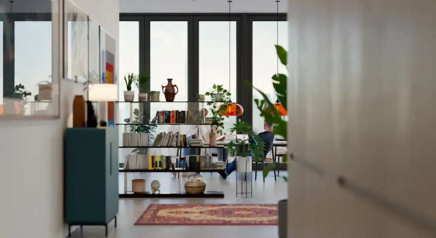 Un salón comedor dos ambientes con estanterías llenas de libros y plantas, y dos personas trabajando en una mesa.