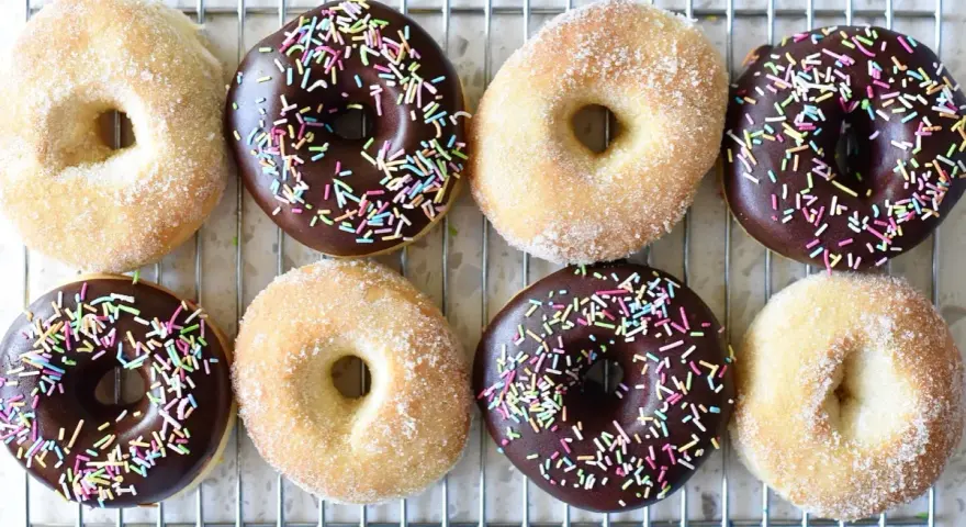 Åtta hemgjorda donuts, vissa med chokladglasyr och strössel, andra med socker. Perfekt för ett donuts recept!