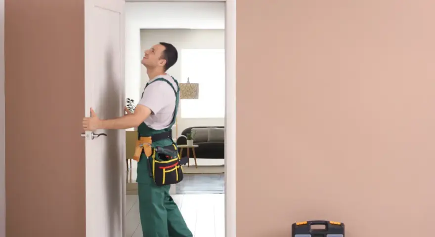 Monter sprawdza wymiary drzwi wewnętrznych, trzymając je w otwartym otworze. Obok stoi skrzynka z narzędziami.