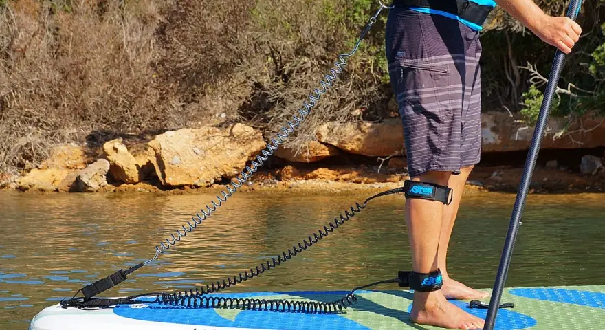 Person befestigt sup leash an Hüfte und Bein für sicheren Stand auf dem Board.
