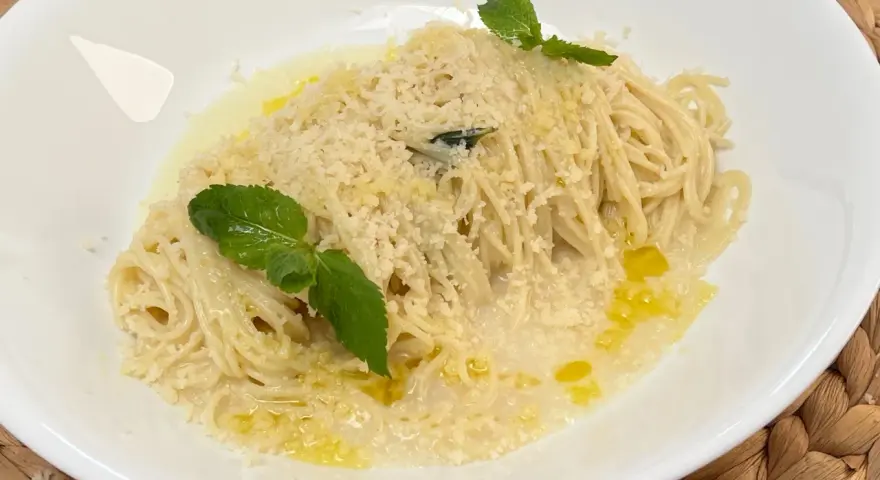 Spaghetti al limone cremosi, conditi con parmigiano e guarniti con foglie di menta fresca.