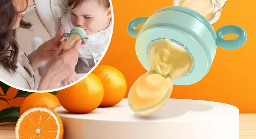 Mama karmi dziecko smoczkiem do owoców, który wygląda jak mały dzbanuszek z pomarańczowym płynem. Obok pomarańcze.