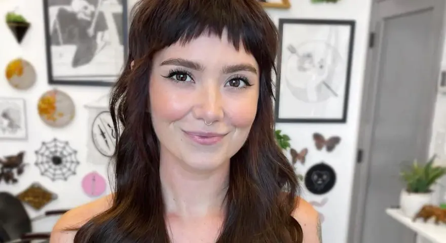 Uśmiechnięta kobieta z ciemnymi włosami i grzywką baby bangs.