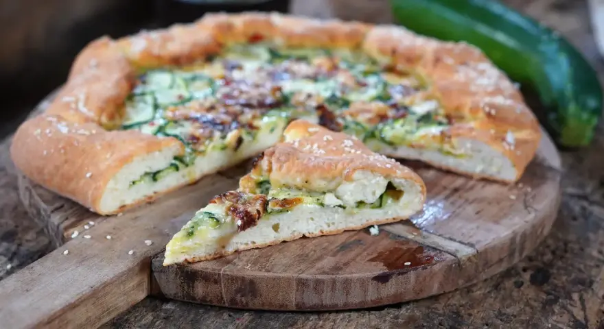 Leckeres Zucchini Pizza Rezept auf einem Holzbrett, mit einem Stück abgetrennt.